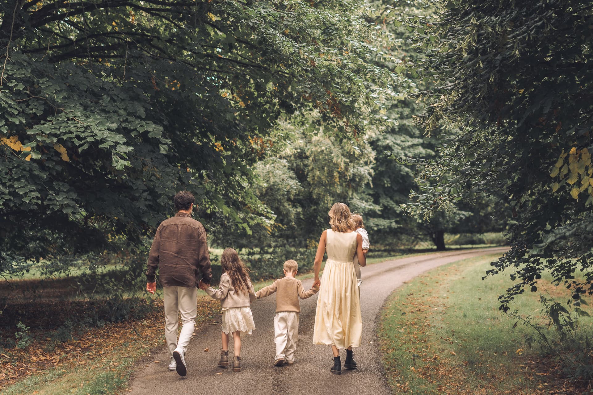 A family of five walking hand in hand down a wooded path