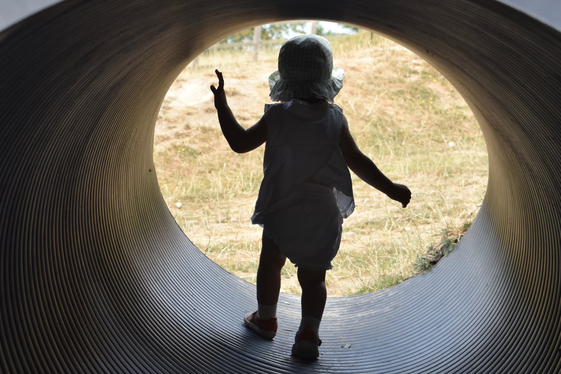 A toddler in a sun hat looking out through a play tunnel